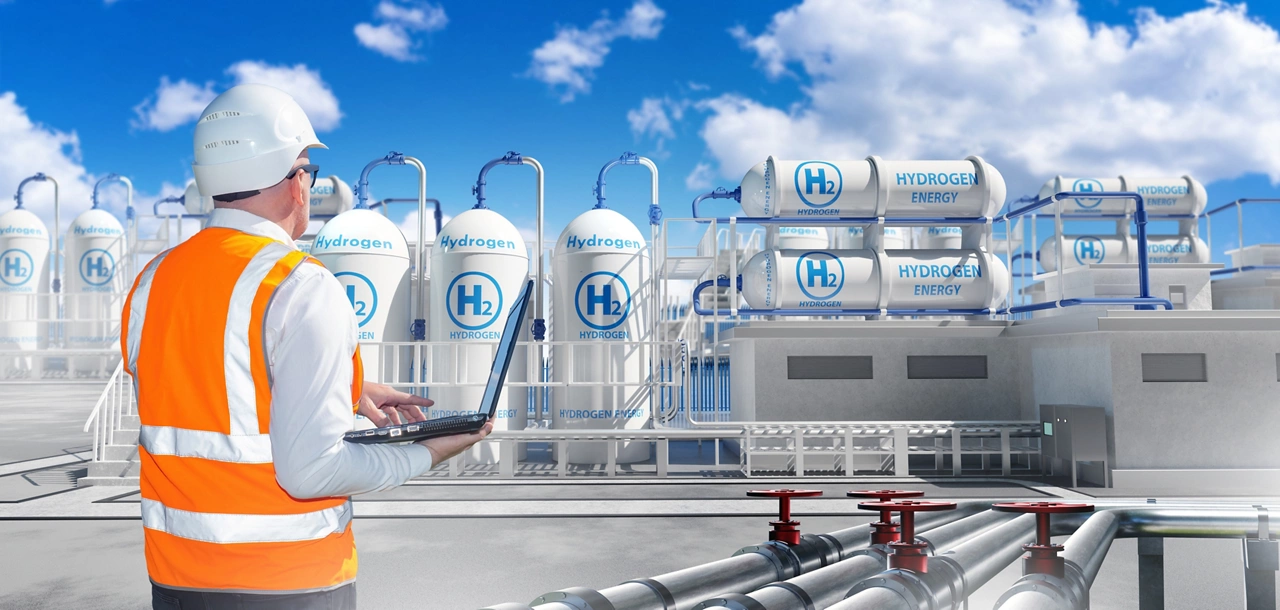 Man near hydrogen power plant. Factory for production of h2 gas. Hydrogen energy. Power plant technologist with laptop. Man inspects hydrogen manufactory. Innovative electrical station on sunny day